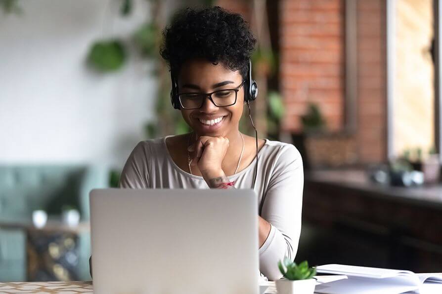Female student wearing headphones smiling at laptop