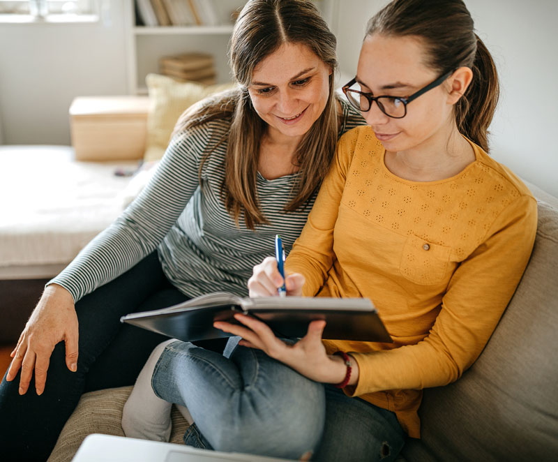 Female student and her mom sitting on a couch working on homework together
